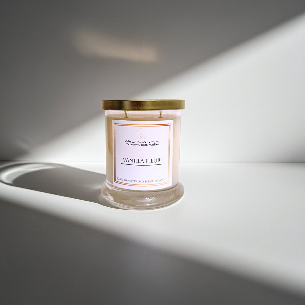 Autumn Moon Candle Vanilla Fleur candle with gold lid with a white background and light shining down