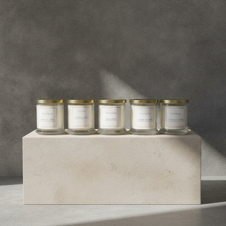 Five Autumn Moon Candle glass jar candles with gold lids and cream labels are lined up on a light stone pedestal against a textured gray wall.