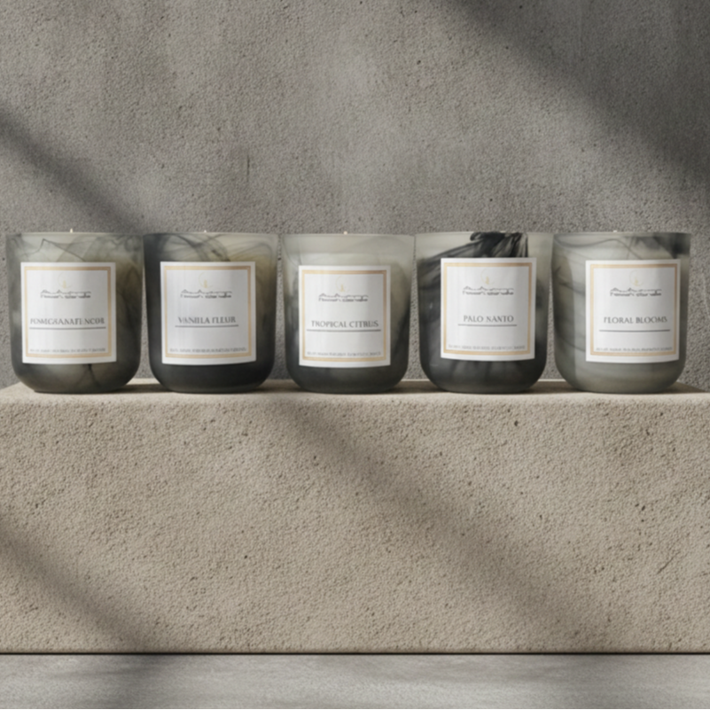 Five Autumn Moon Candle jar candles with white labels are lined up on a textured stone block against a concrete wall, with soft diagonal shadows across the scene.